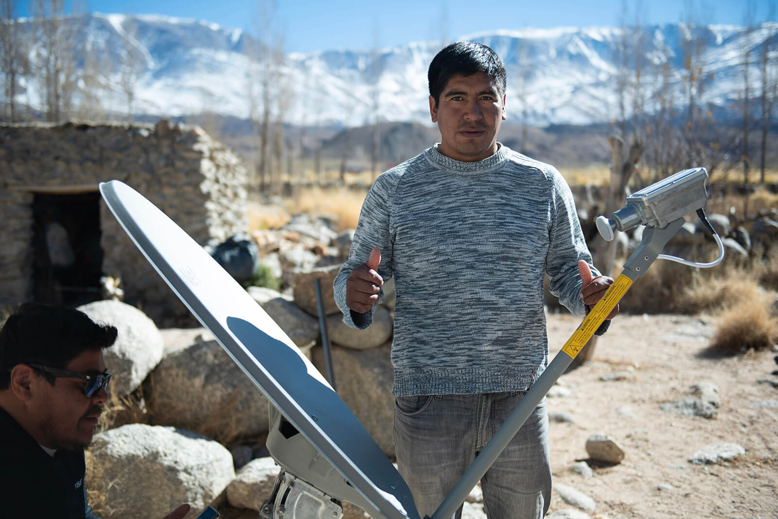 Ciudadano rural contento, sostiene la antena de internet que está instalando un técnico de Arsat.