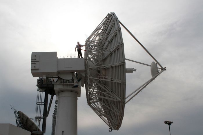 Un ingeniero está a lo alto y por detrás de la antena parabólica mayor, en la Estación Terrena de Benavídez, para trabajos de reacondicionamiento.