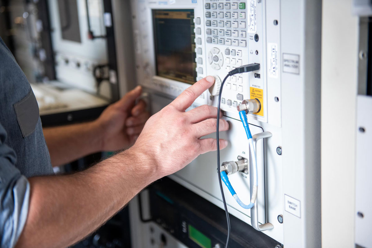 Primer plano de las manos de un técnico que toca unas perillas sobre un equipo de control y monitoreo satelital en la Estación Terrena de Benavídez.