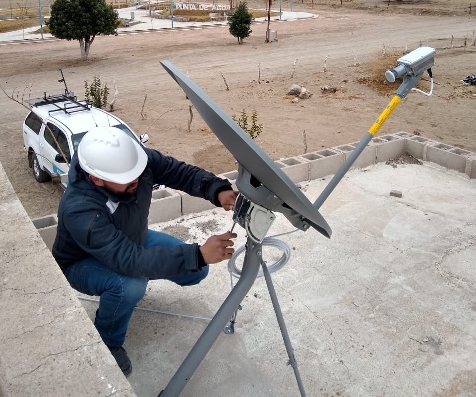 Un técnico instala una antena de internet sobre el techo de un establecimiento en una zona rural.