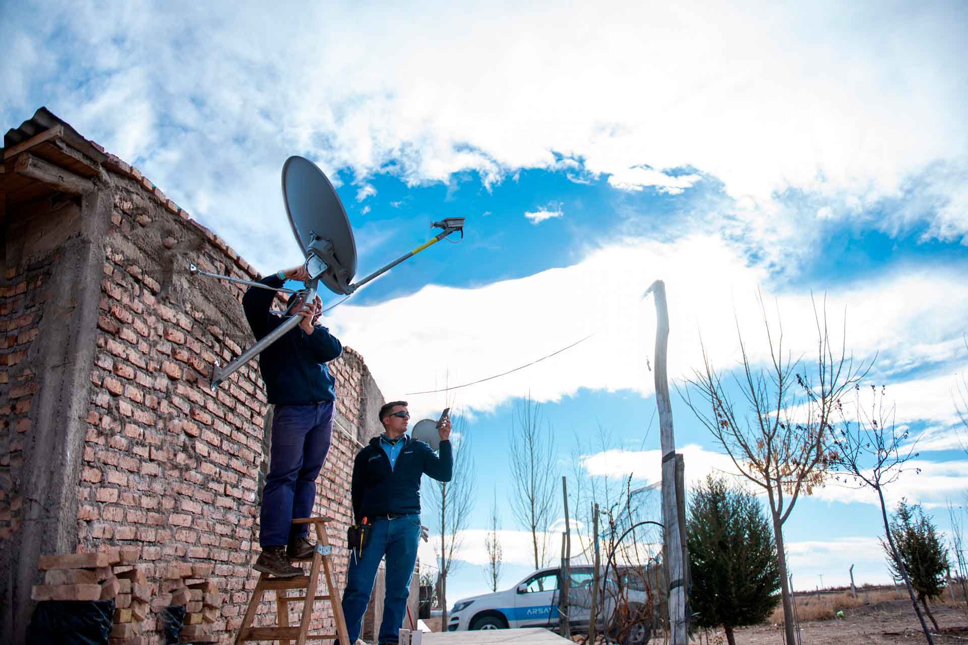Dos técnicos instalan una antena de internet en un hogar de una zona rural.